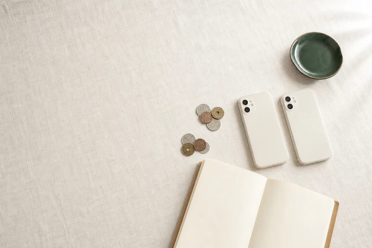 並べた2台のスマートフォンと白紙のノート、2つに分けた小銭